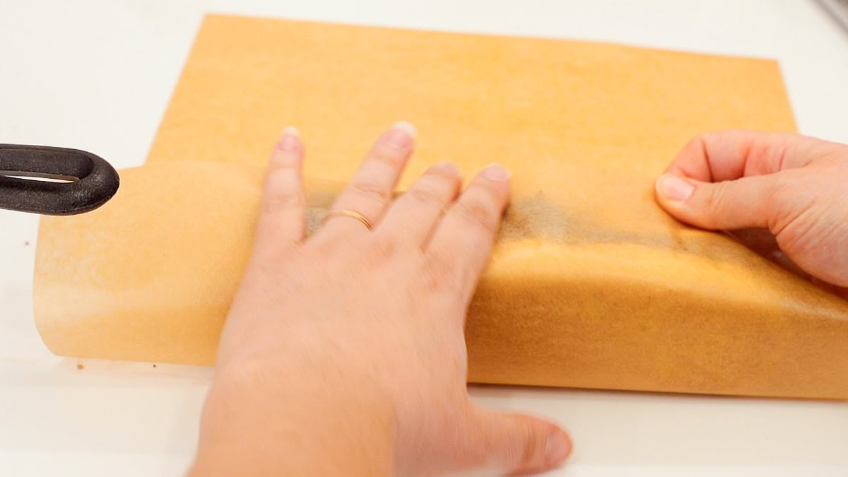 hands rolling ground beef cheesesteak in a piece of parchment paper.