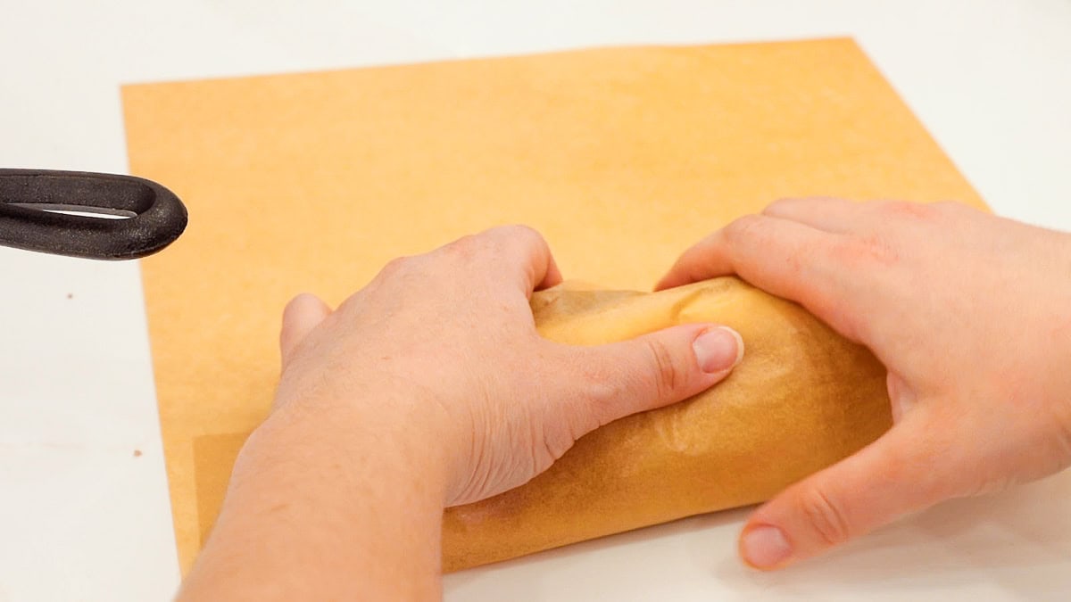 hands rolling up ground beef cheesesteak in a piece of parchment paper.