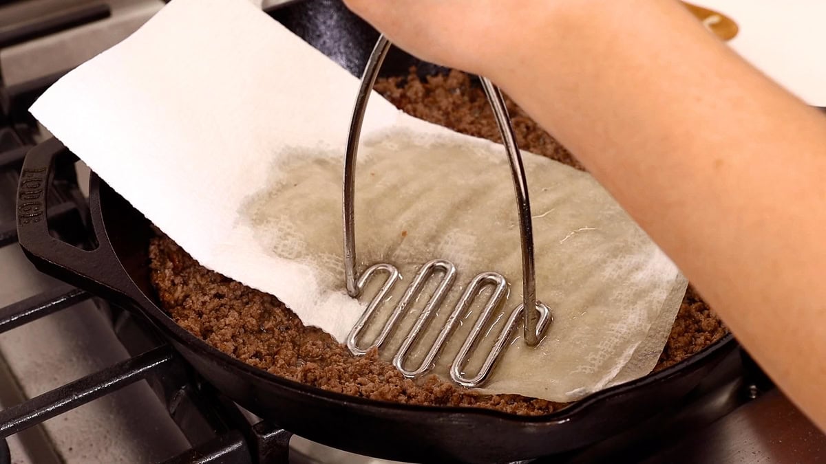 removing grease from ground beef in skillet with paper towel.