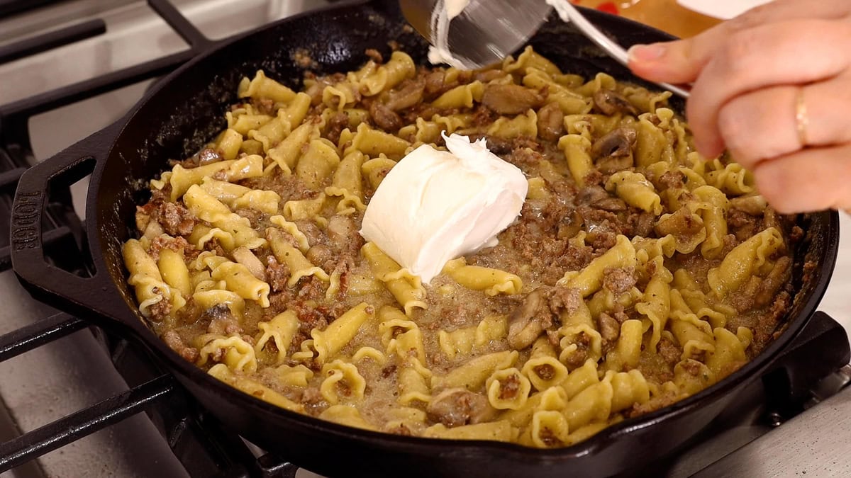 adding sour cream to ground beef stroganoff in skillet.