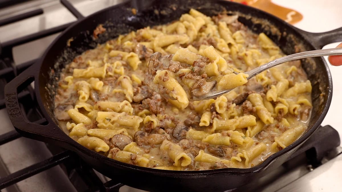 close up of cooked ground beef stroganoff in a skillet with scoop showing the finished meal.