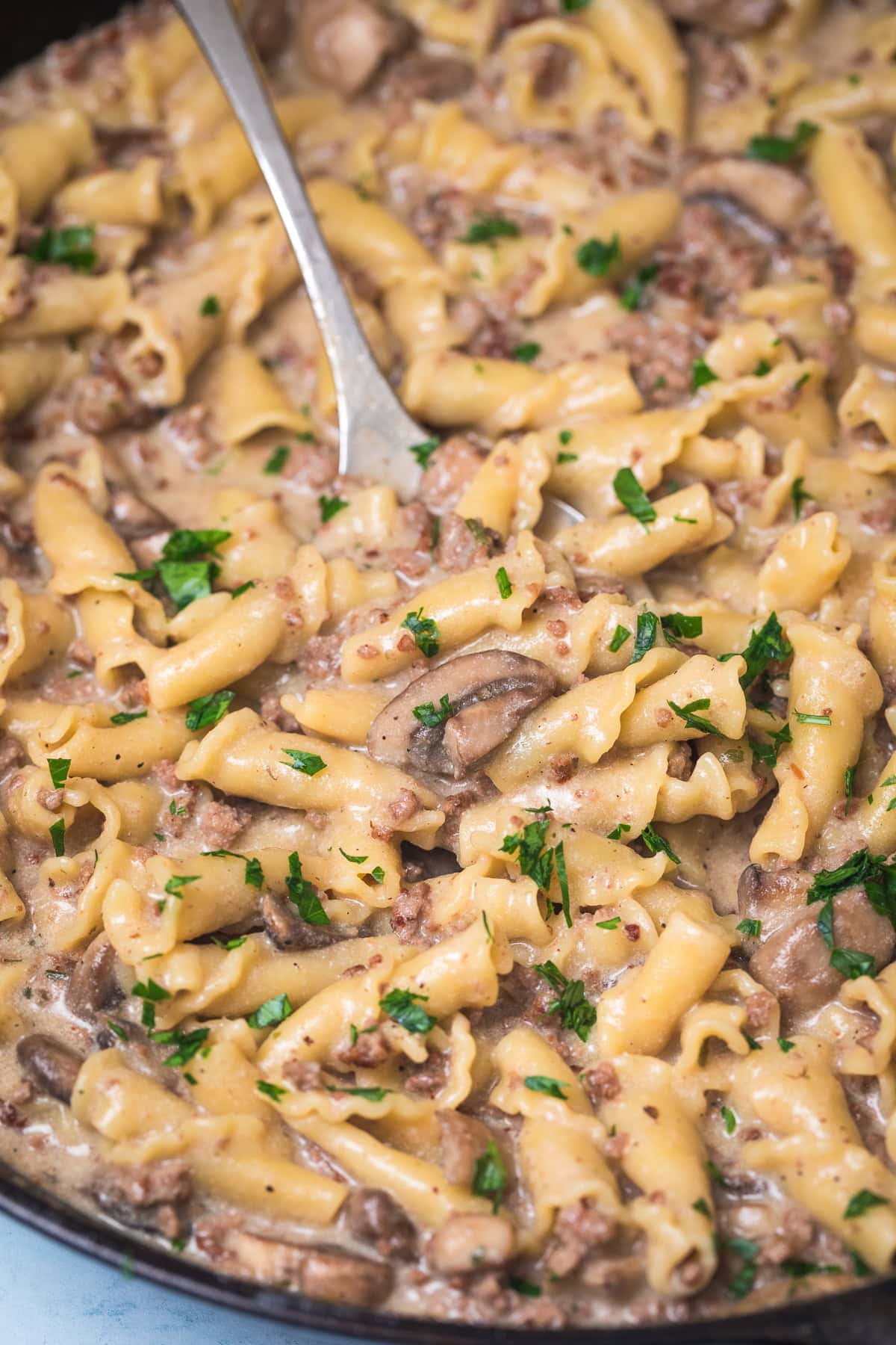 ground beef stroganoff in a cast iron pan with a metal serving spoon.