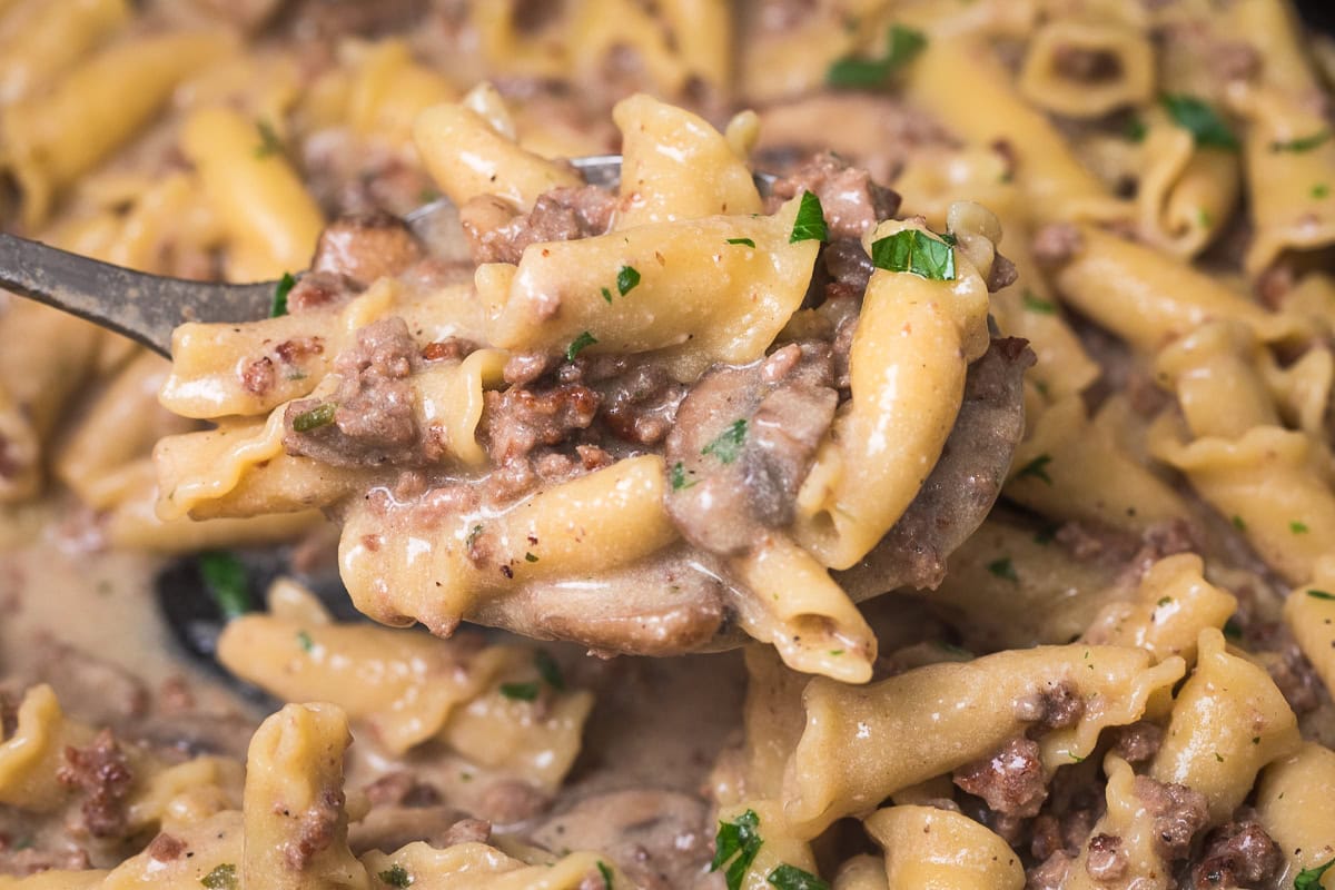 close up of ground beef stroganoff on a spoon in a cast iron skillet.