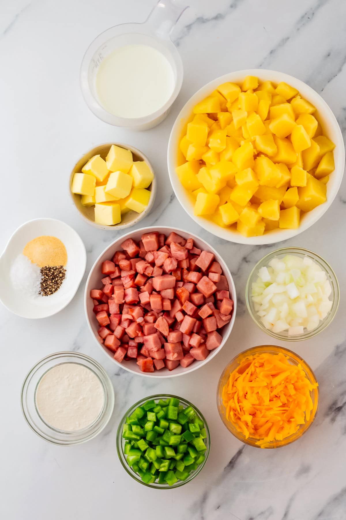 ingredients in bowls for ham and potato casserole, ham, potatoes, butter, onions, cheese, peppers, milk, seasonings, flour.