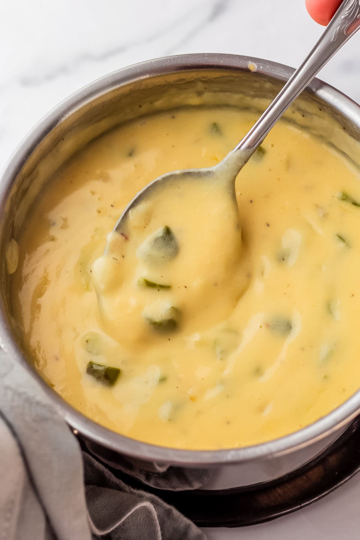 spoon showing cheese sauce with peppers and onions in a sauce pan.