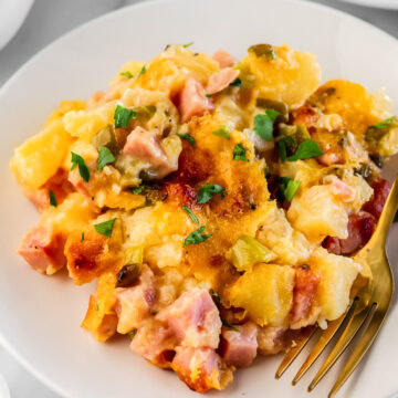 ham and cheese casserole on a white plate with a gold fork.