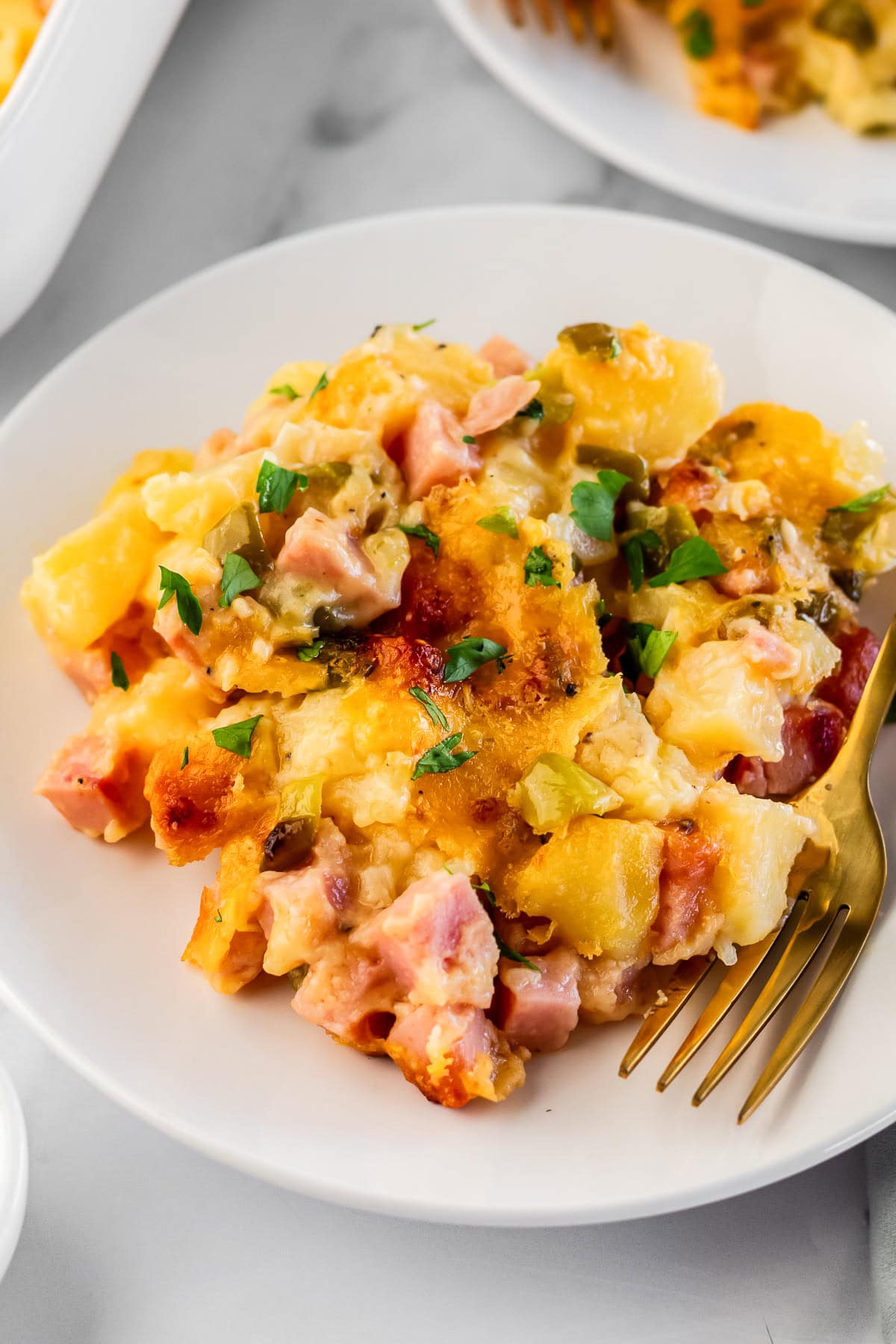 ham and cheese casserole on a white plate with a gold fork.