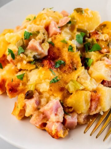 ham and potato casserole on a white plate with a gold fork.