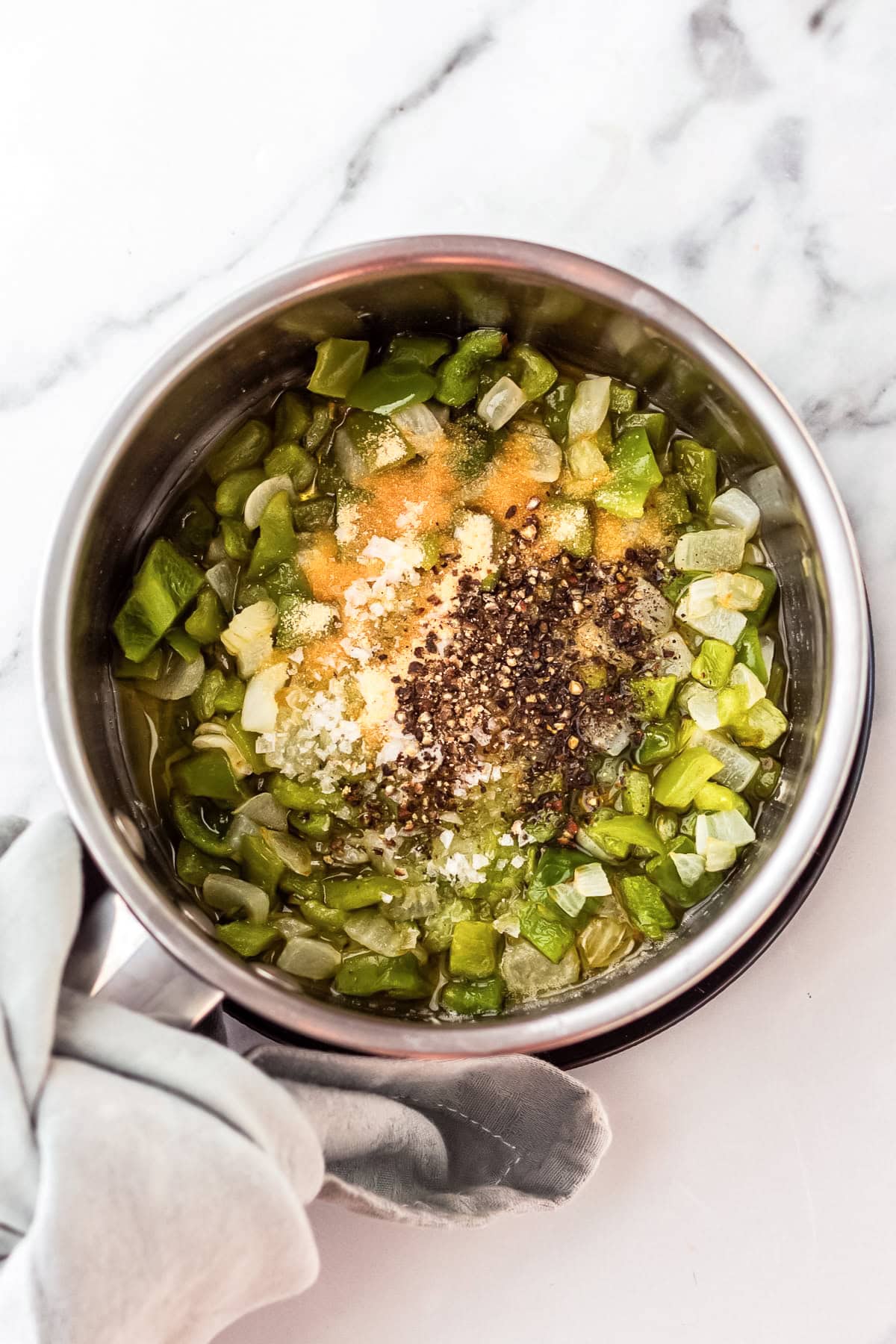 seasonings added to peppers and onions in a saucepan.