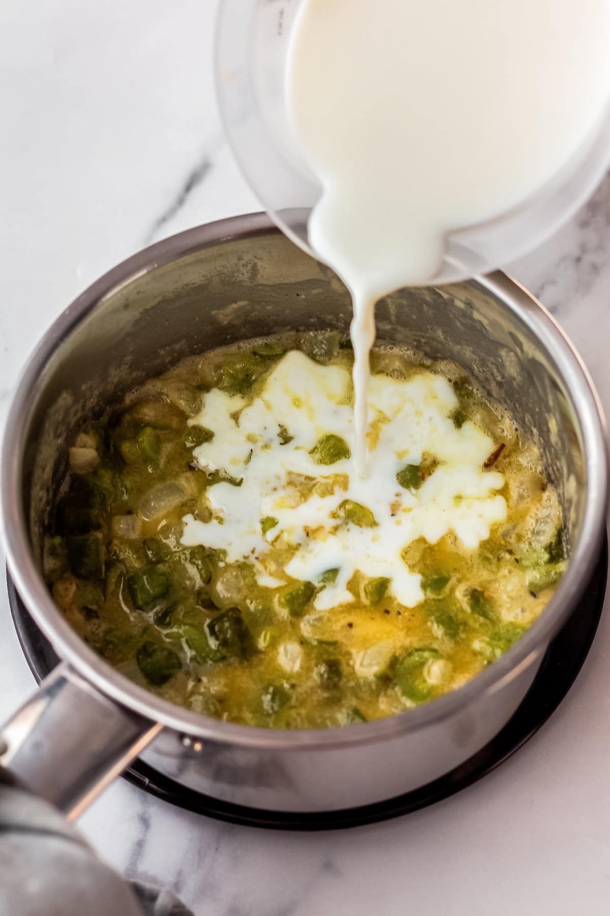 milk being poured into pepper and onion mixture thickened with flour.