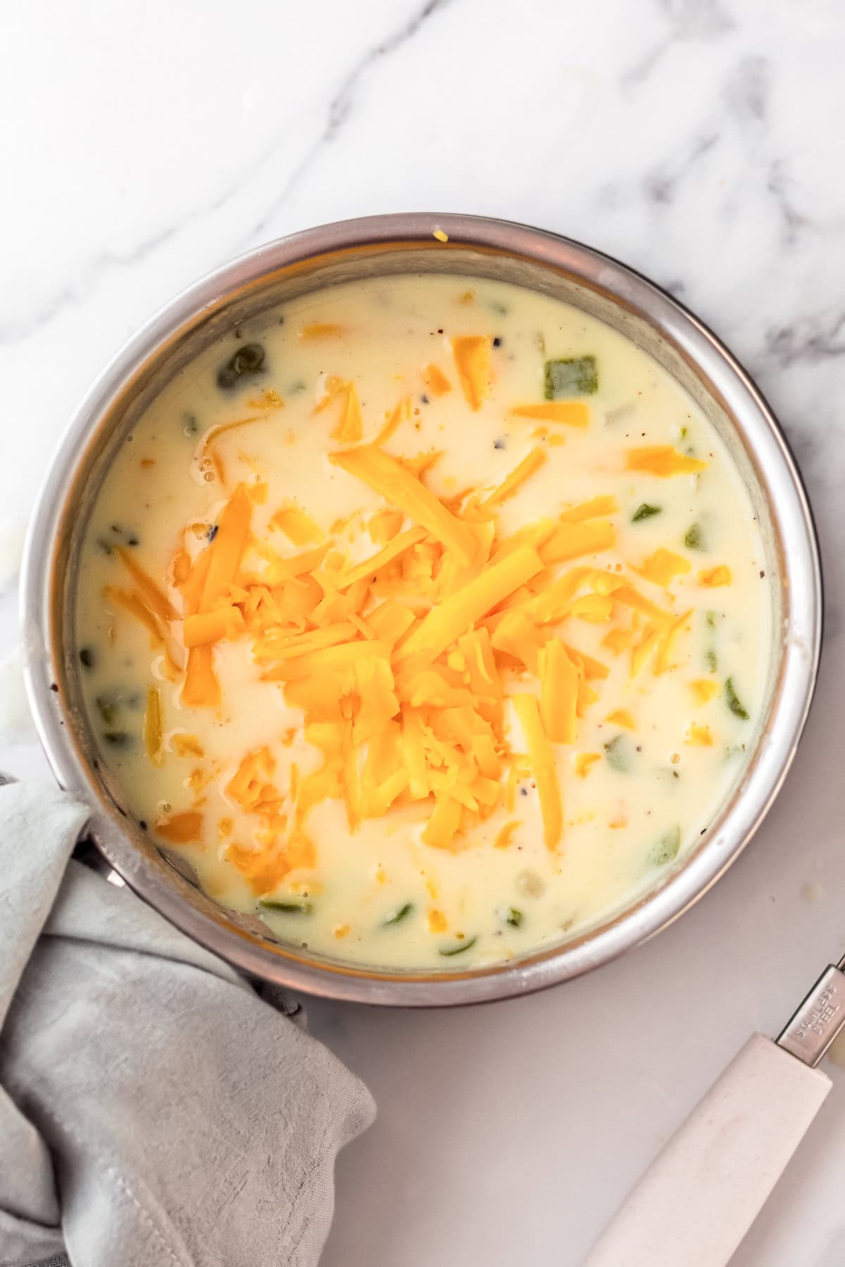 cheese being added to roux sauce with peppers and onions.