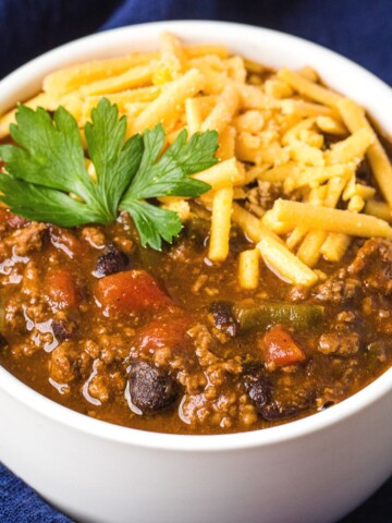 instant pot chili with shredded cheddar and garnish in a white bowl on a navy blue napkin.