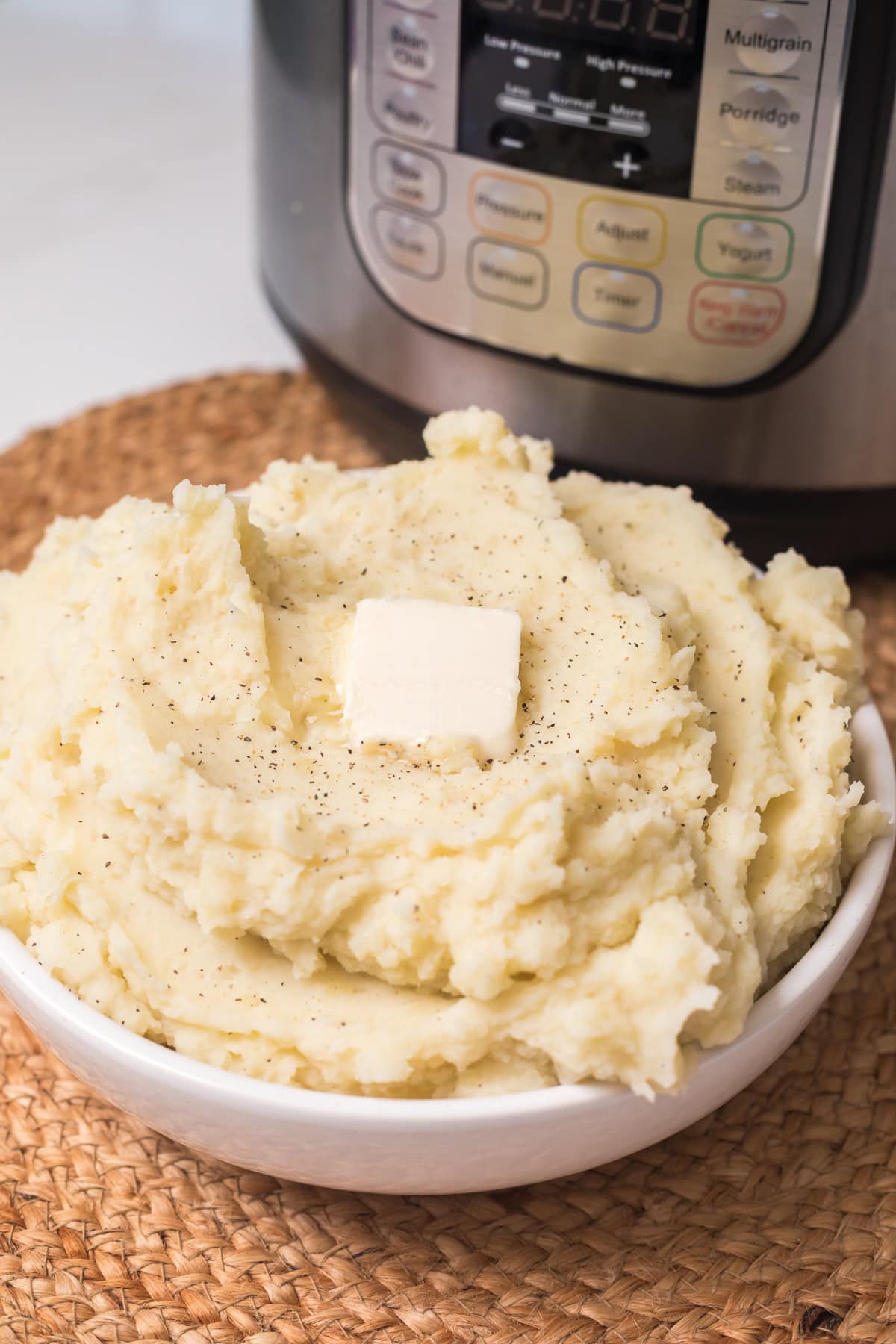 mashed potatoes in a white bowl with a tab of butter on the top and instant pot behind it.