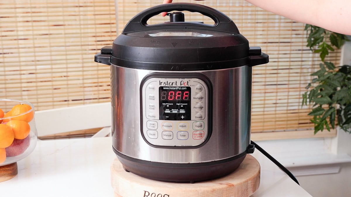 photo of an instant pot on a boos cutting board on quartz countertop with hand pushing the sealing valve. on the instant pot.