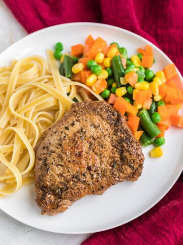 instant pot pork chop on a plate with noodles and mixed veggies.