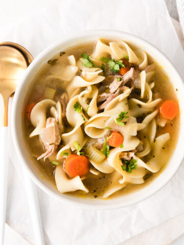 turkey noodle soup in a bowl with spoons to the left