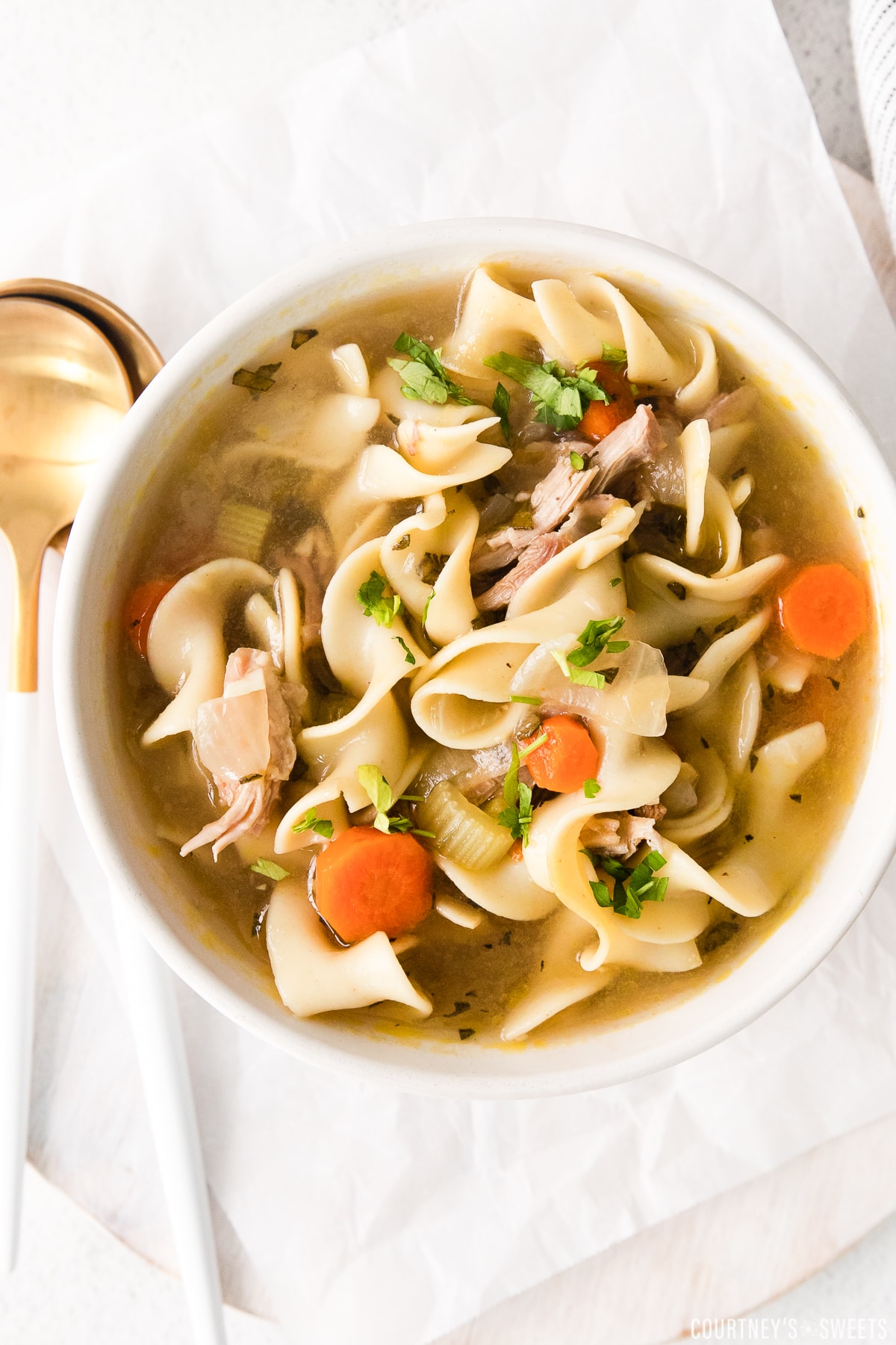 turkey noodle soup in a bowl with spoons to the left