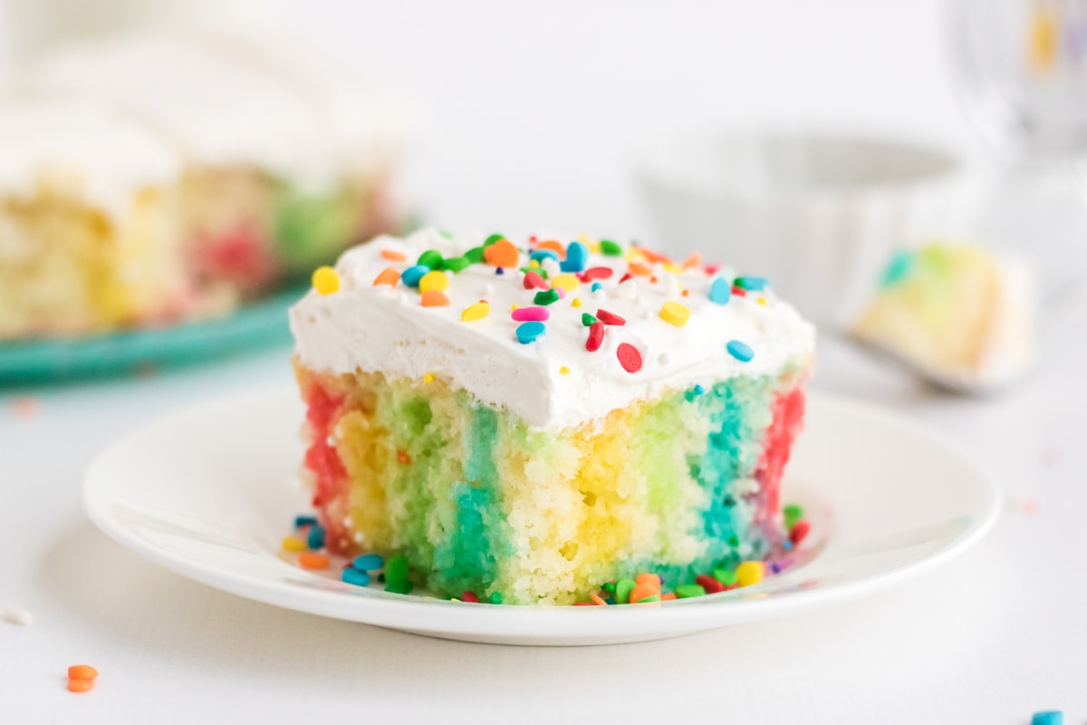 rainbow jello poke cake on a white plate.