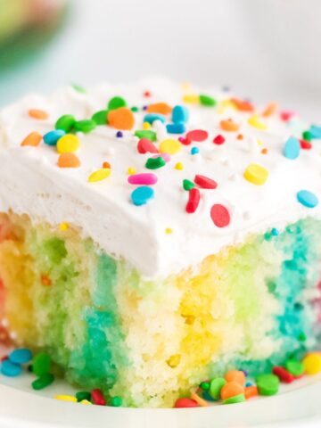 jello poke cake on a white plate with rainbow sprinkles.