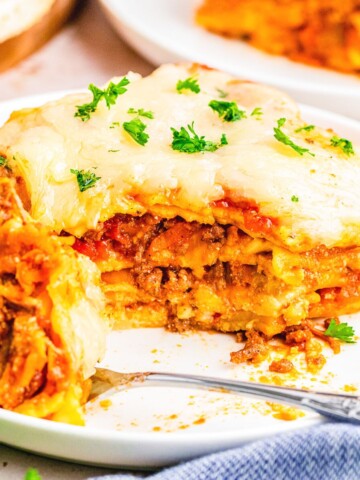 lasagna bolognese on a plate with a fork and bite full taken out of it.