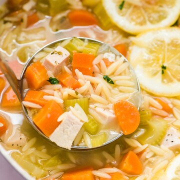 lemon chicken orzo soup in a ladle with pot