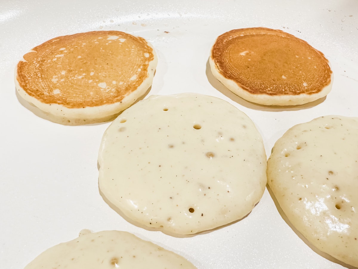 pancakes cooking on a skillet with bubbles on top of the pancakes to show they're ready to flip.