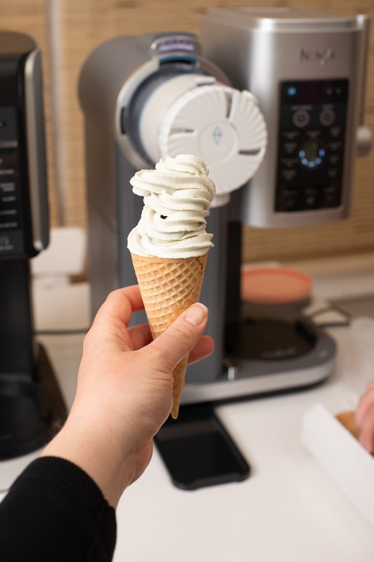 hand holding a cone with mint chocolate chip ice cream in it made in the ninja swirl by creami with the ninja swirl behind it.