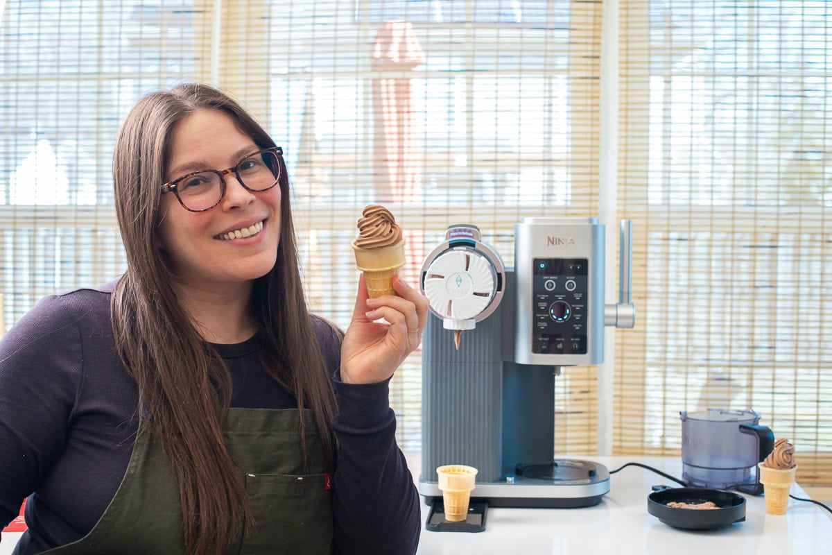 Courtney of Courtney's Sweets holding a chocolate soft serve ice cream cone made by the Ninja Swirl with the Ninja Swirl to the right behind her on the counter.