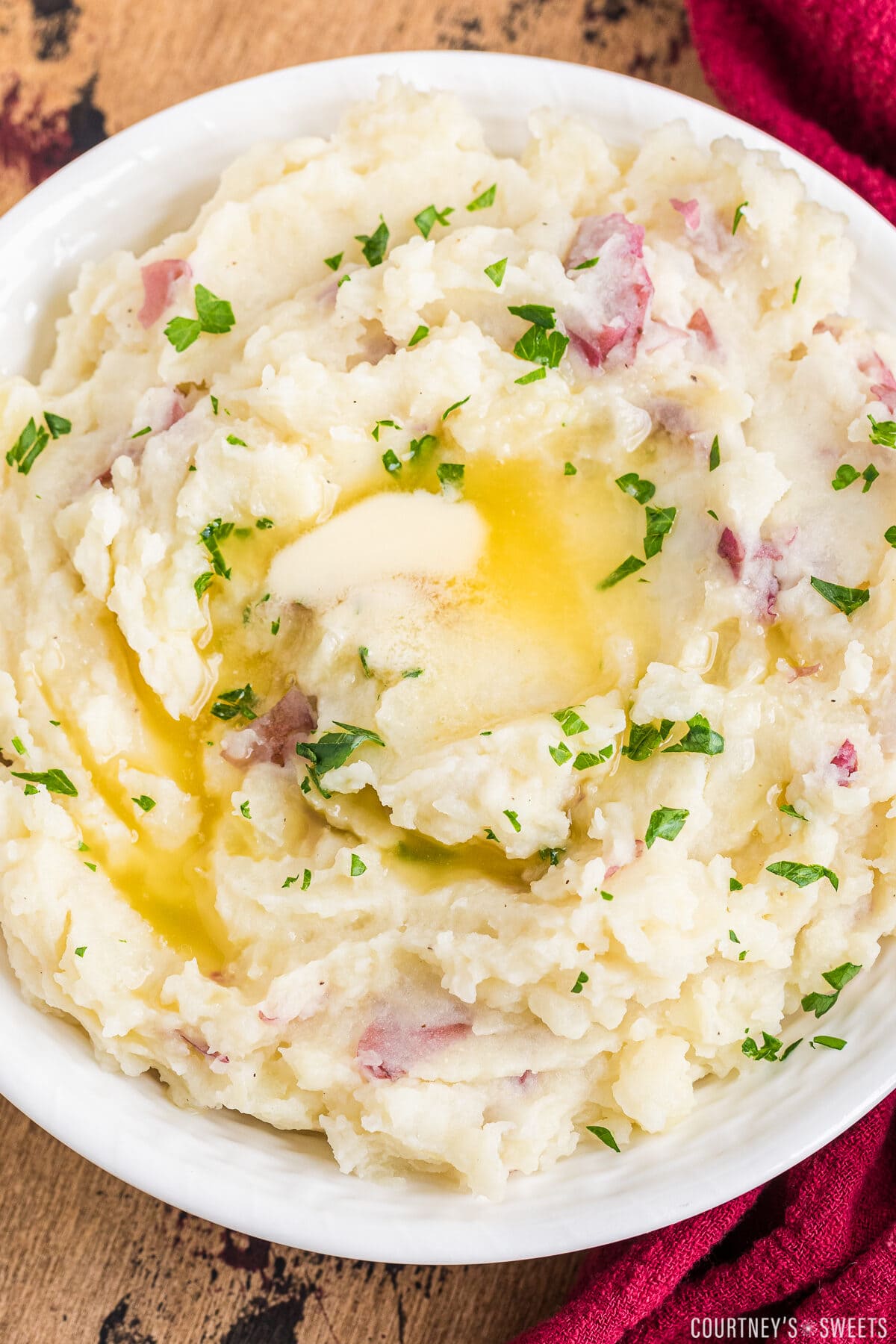 red skin mashed potatoes in a white bowl with melted butter and chopped parsley for garnish.