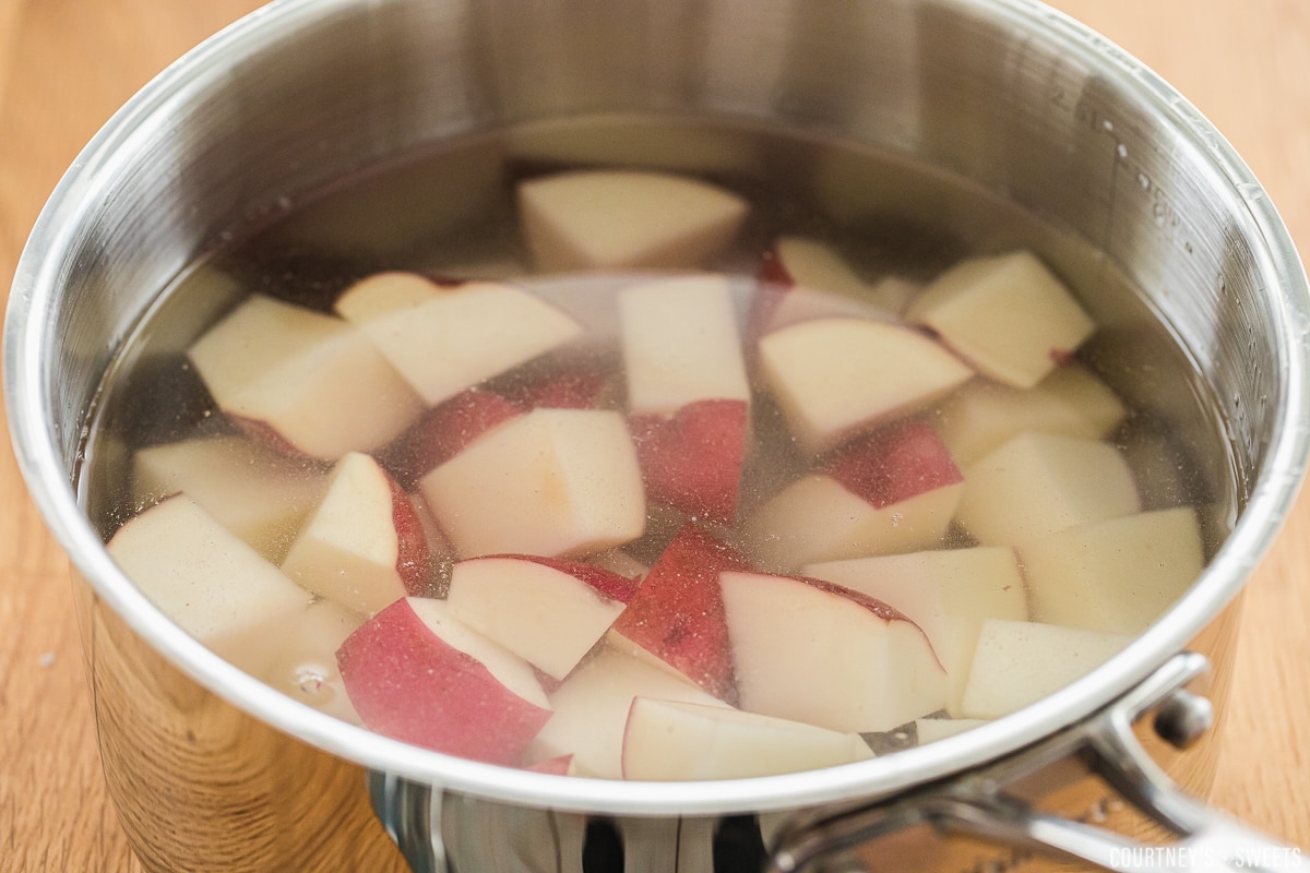 red skinned potatoes chopped in a saucepan with water covering them.