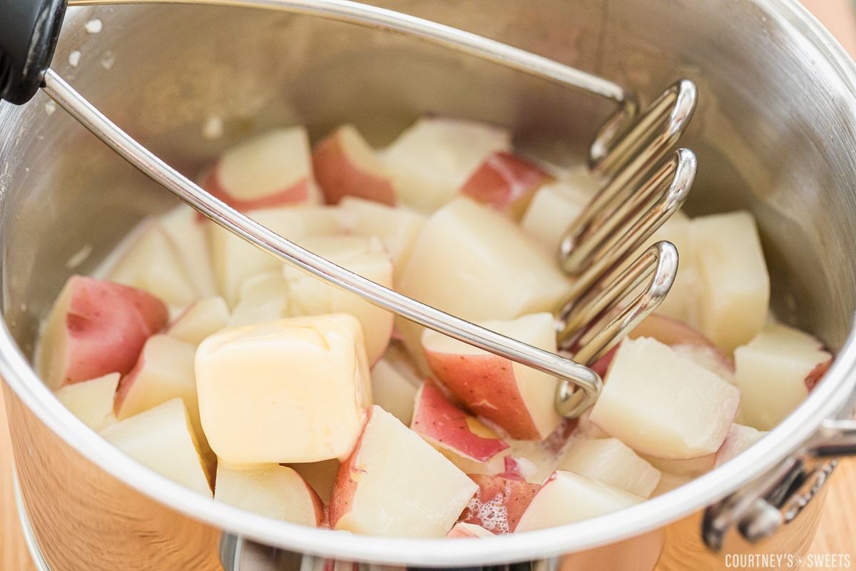 drained potatoes for mashing in a saucepan with a potato masher.