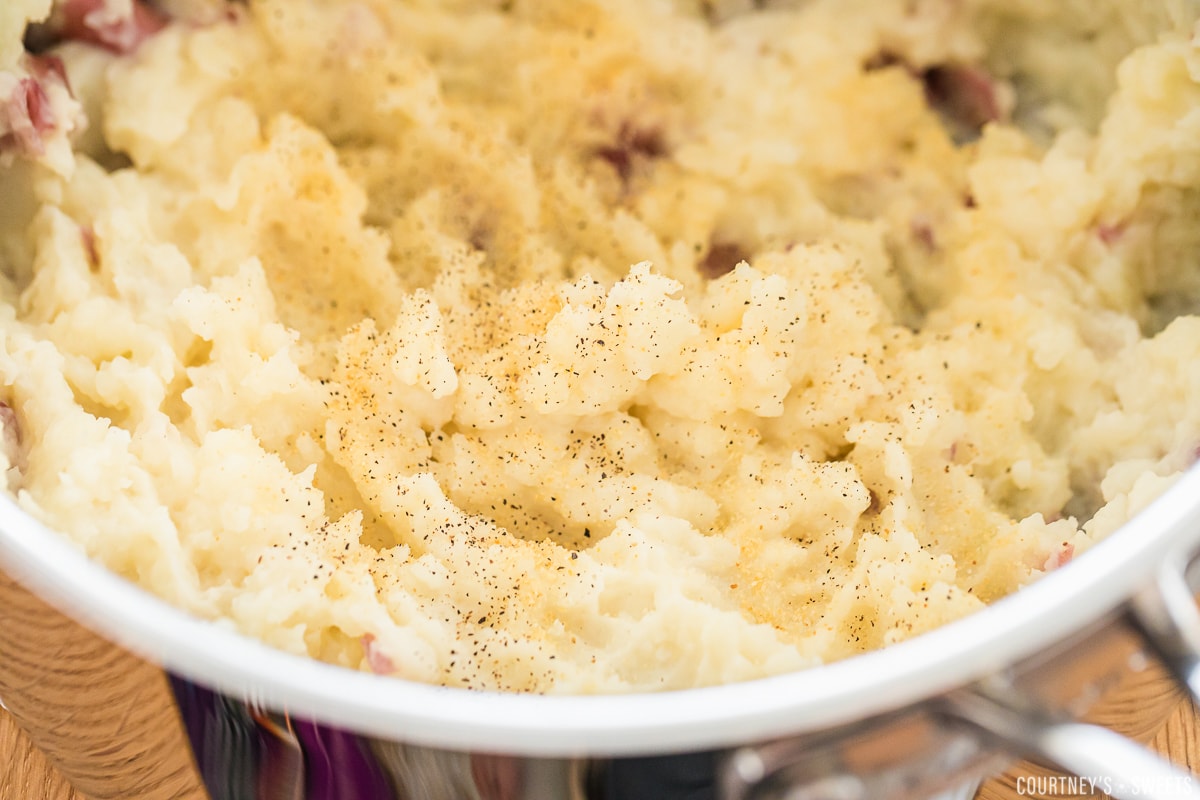 seasoning mashed potatoes in a saucepan.