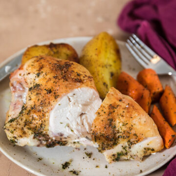 sliced open roasted split chicken breast on plate with roasted carrots and potatoes