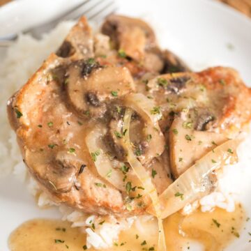 slow cooker bone in pork chops on a plate with mushrooms and onions over white rice.