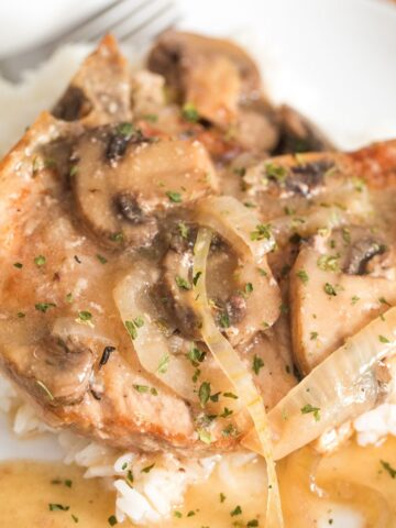 slow cooker bone in pork chops on a plate with mushrooms and onions over white rice.