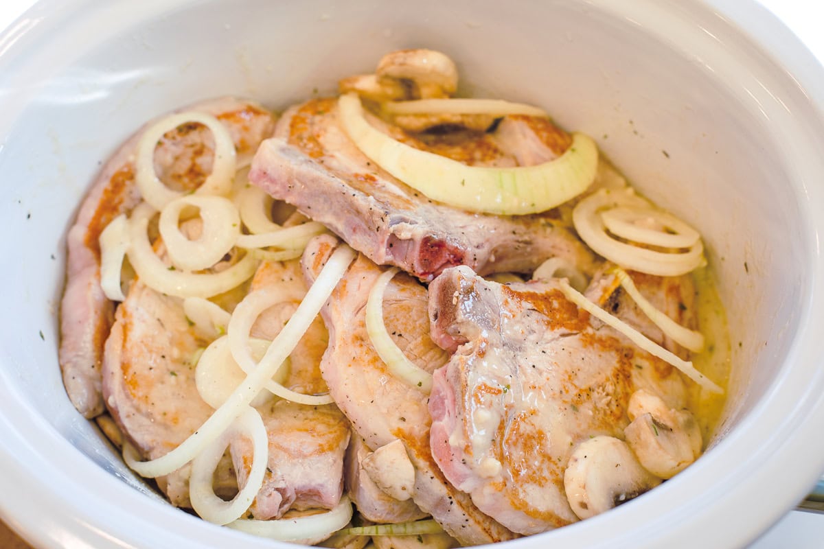 seared raw bone in pork chops in a slow cooker with onions and mushrooms.