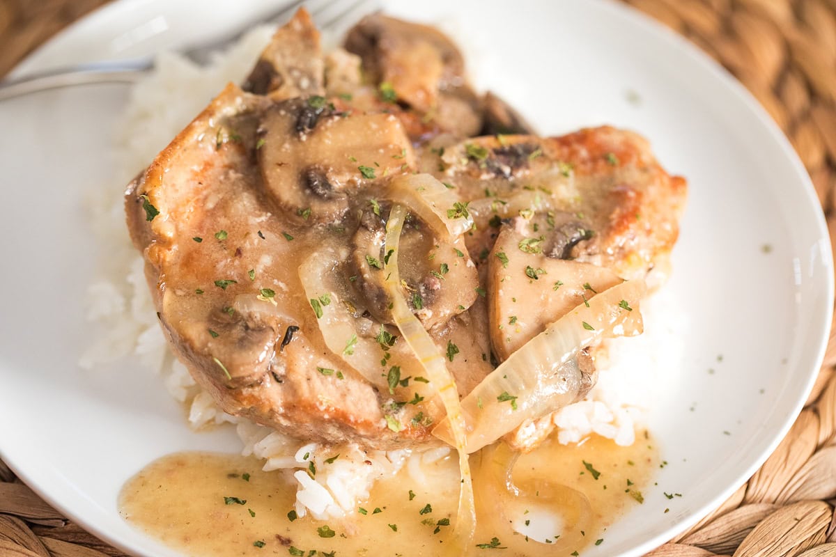 plate with slow cooked pork chop with mushrooms and onions over rice on a white plate.