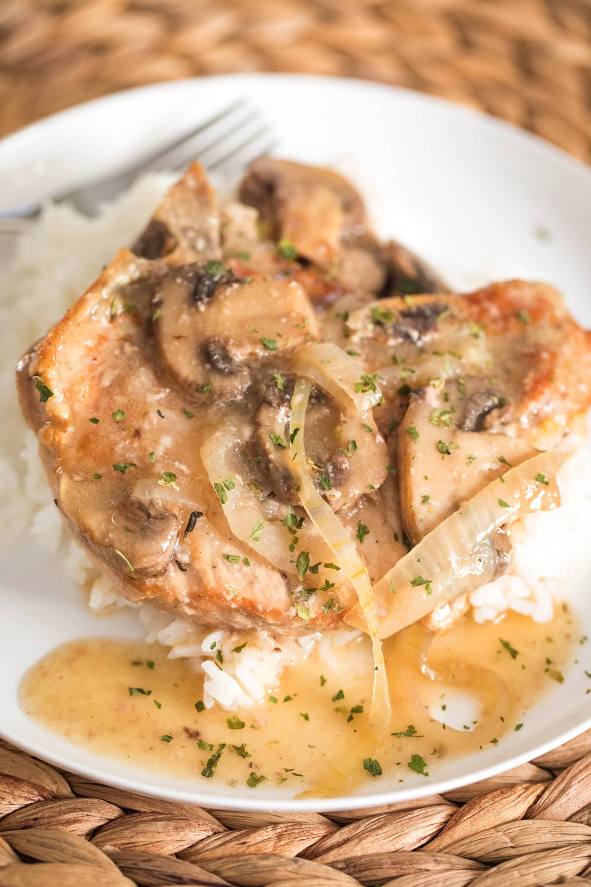 slow cooker bone in pork chop smothered with onions and mushrooms over rice on a white plate.