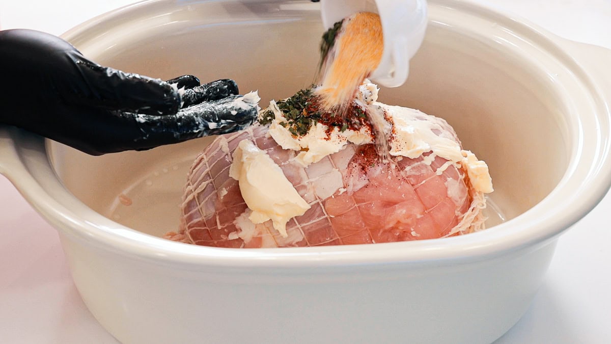 adding seasonings to a buttered turkey breast in a slow cooker crock.