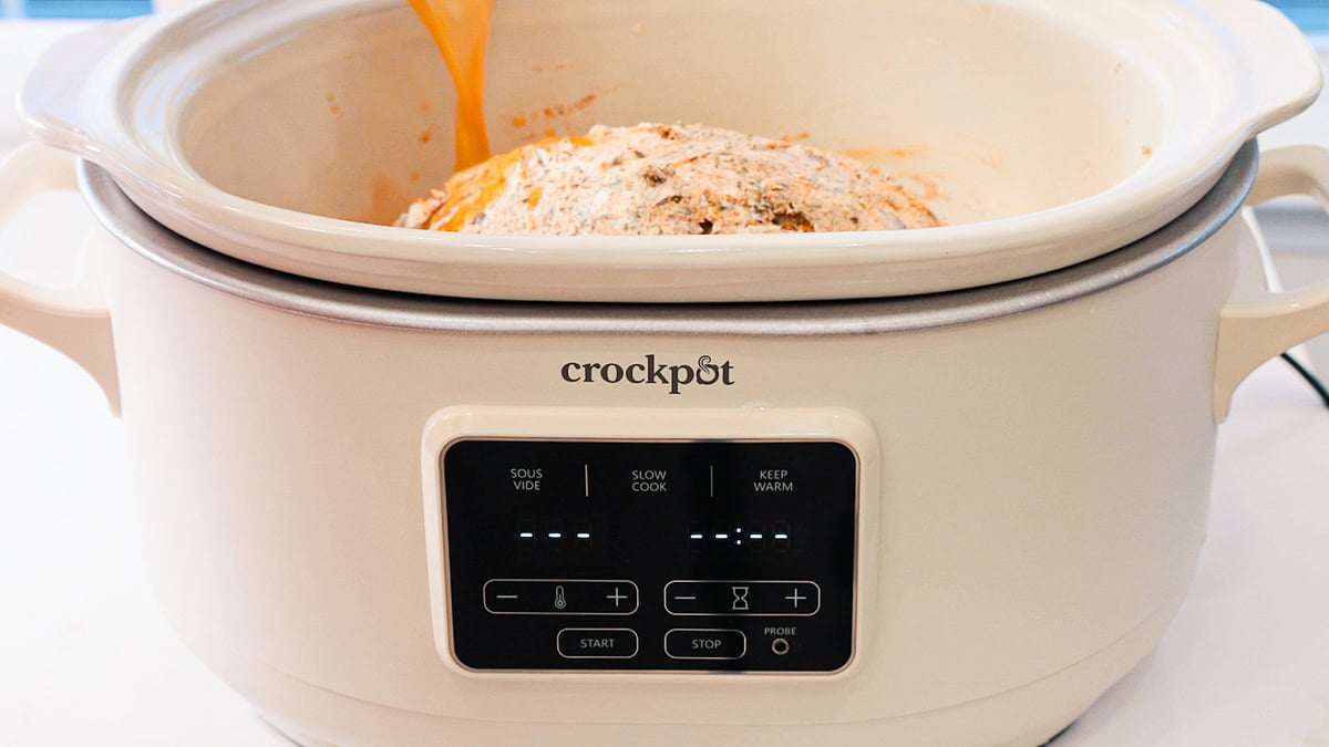 broth being poured into a slow cooker with a buttered and seasoned boneless turkey breast roast.