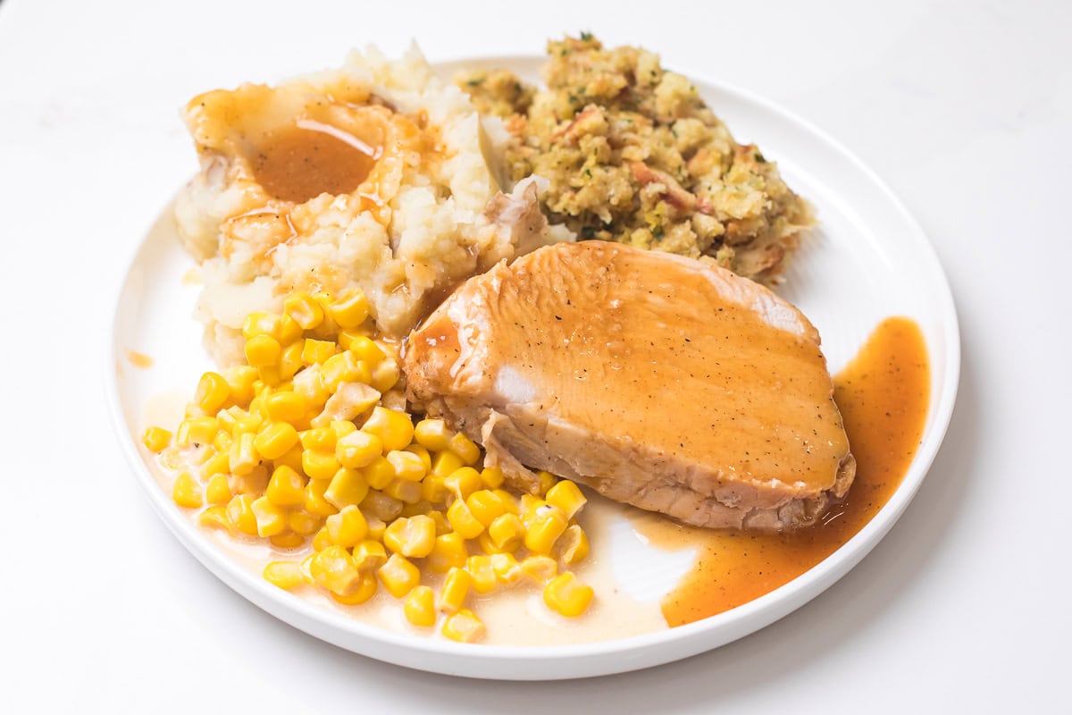 turkey dinner on a plate, mashed potatoes with gravy, stuffing, buttered corn, and slow cooker boneless turkey breast.