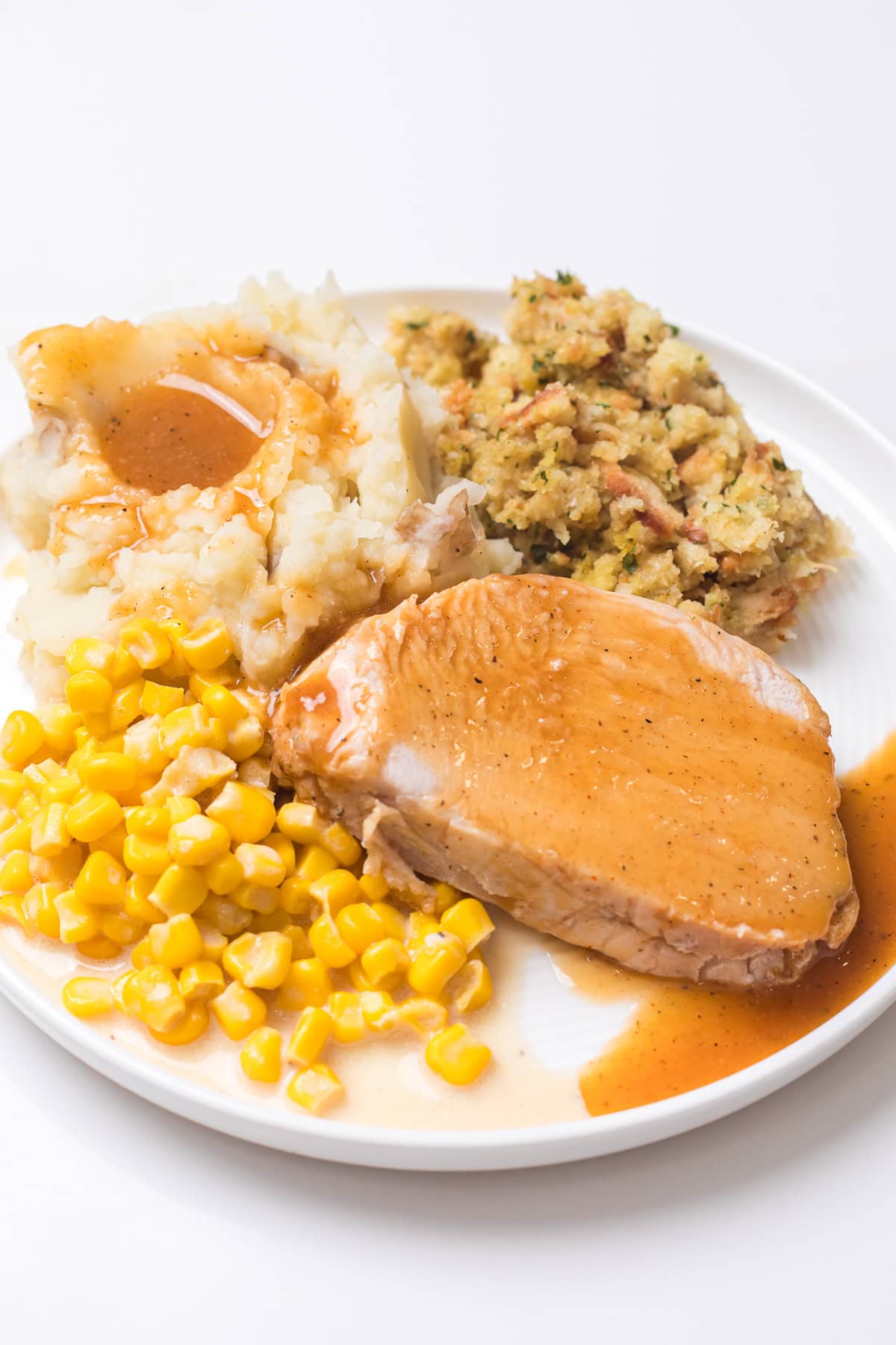 a slice of slow cooker boneless turkey roast on a plate with gravy, mashed potatoes, corn, and stuffing.