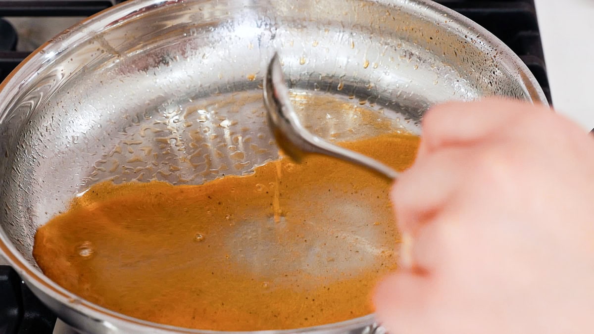 adding broth with a teaspoon to a skillet.