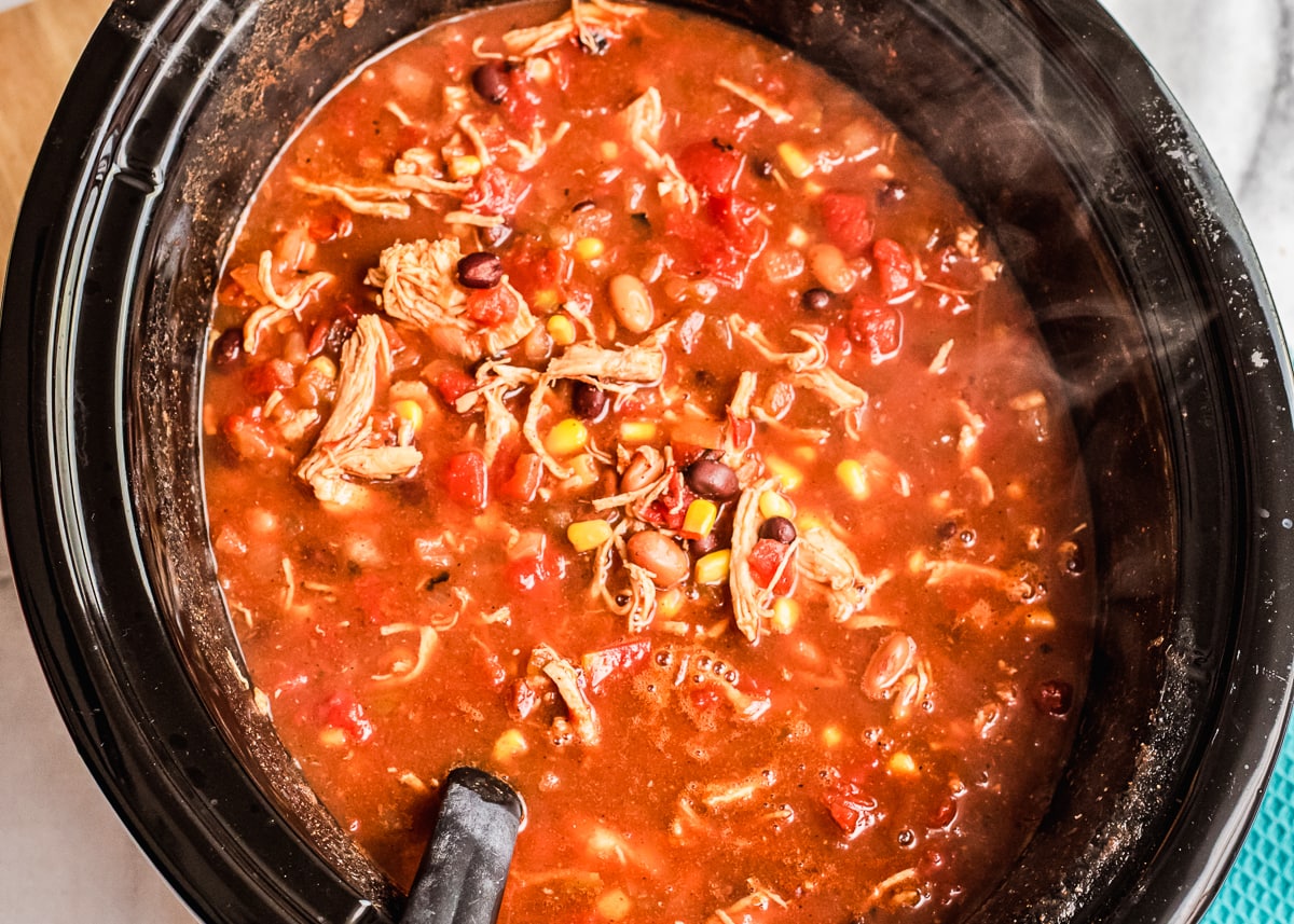 slow cooker chicken taco soup cooked in a crock pot with a spoon mixing.