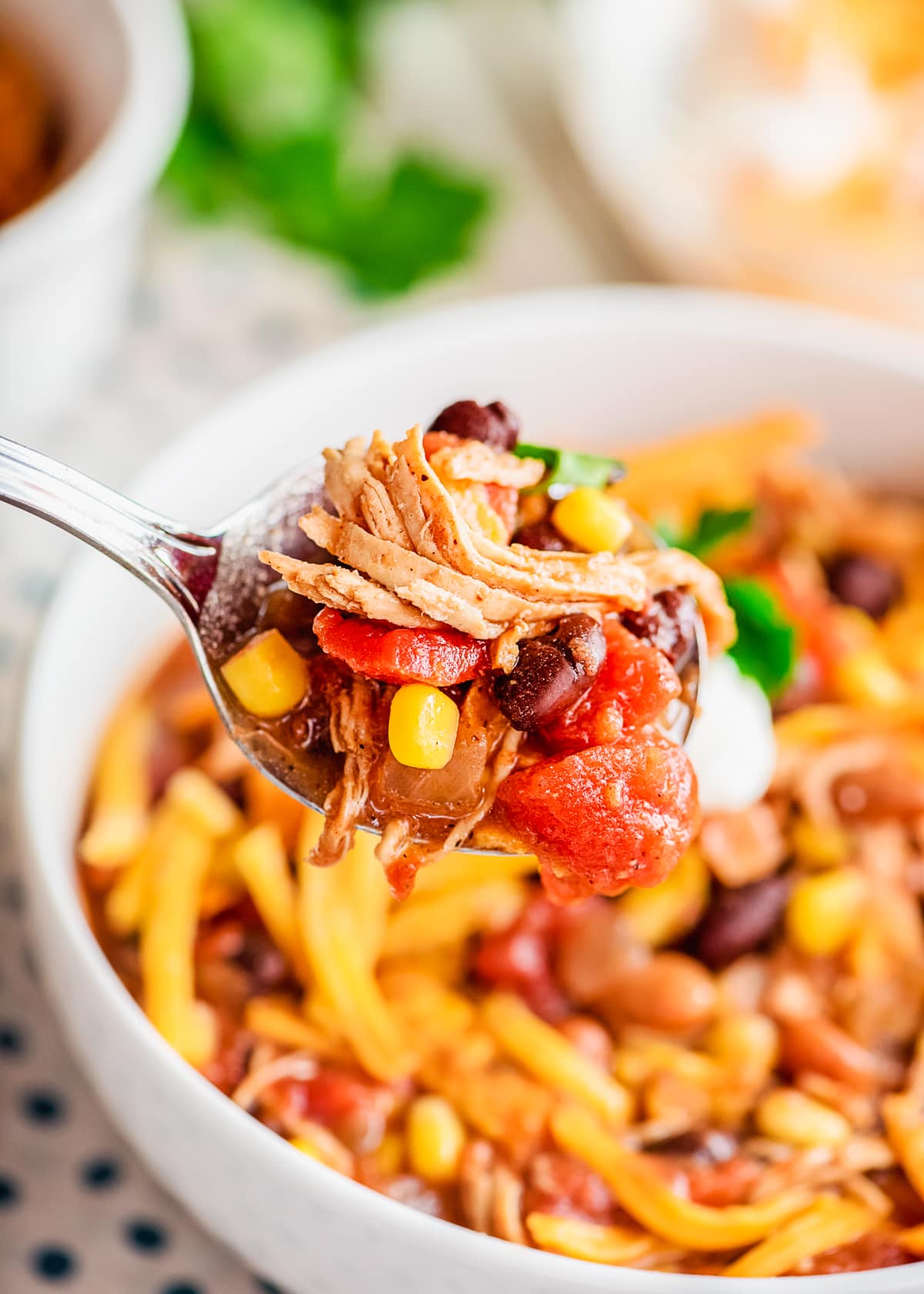 spoon holding a bite of chicken taco soup above a bowl full.