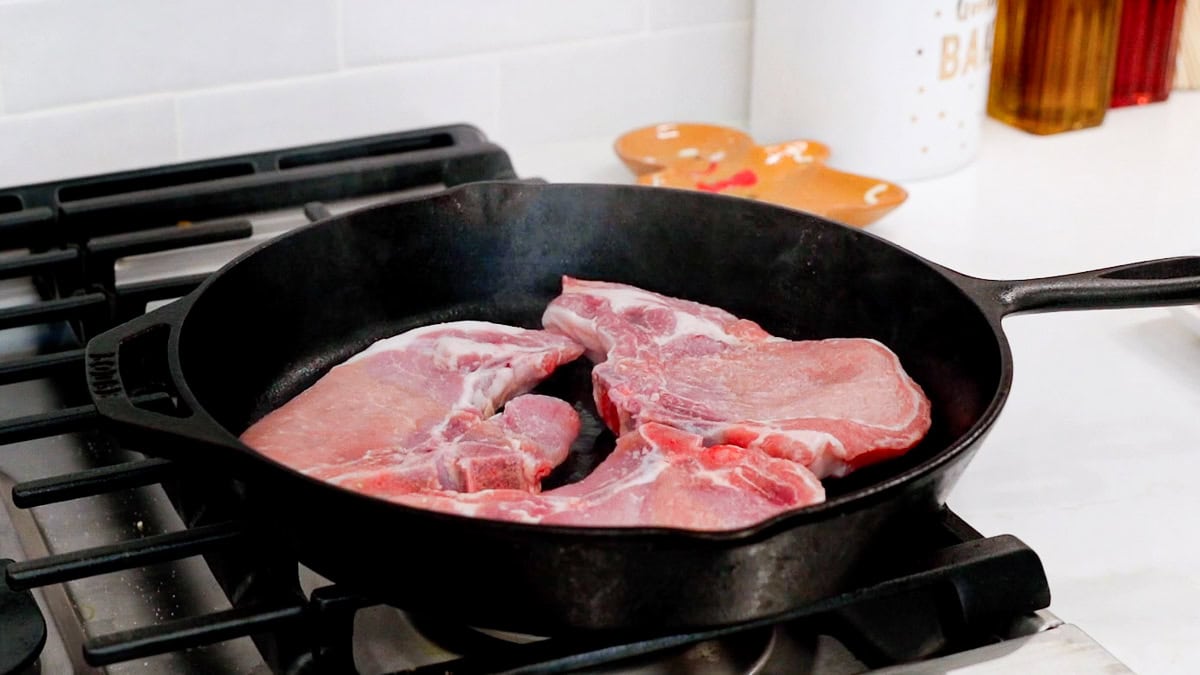 raw pork chops browning in a cast iron skillet.