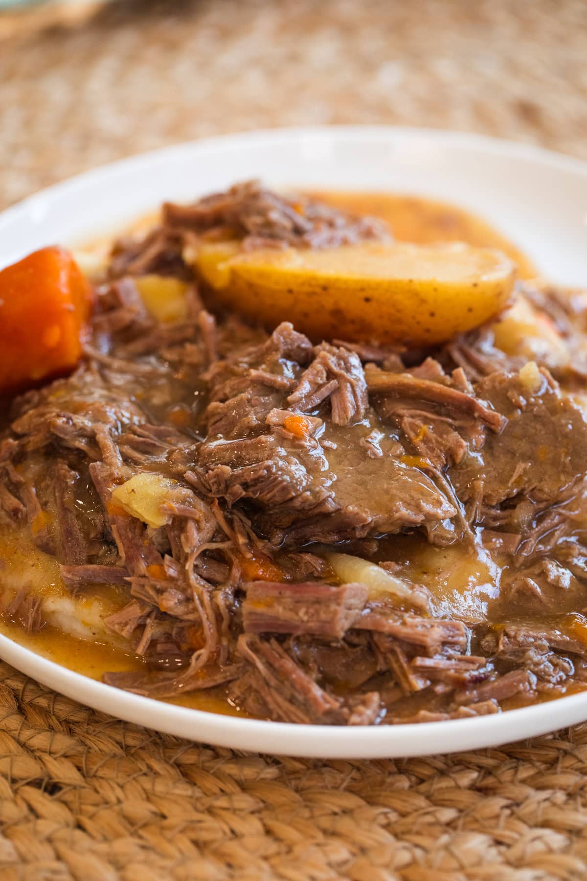 slow cooker bottom round roast over mashed potatoes with potatoes and carrots on a white plate.