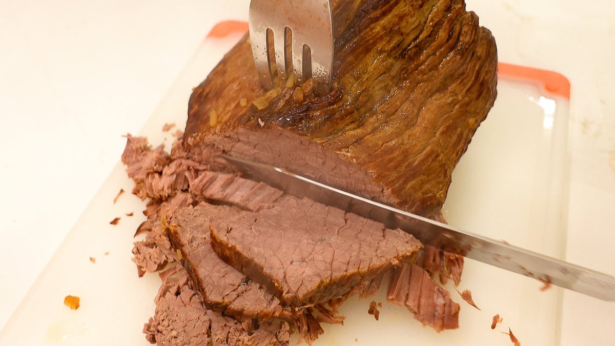 top round roast being sliced on a cutting board.