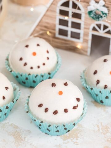 snowman hot chocolate with little christmas house behind itbombs in blue and black polka dot muffin liners