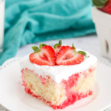 strawberry poke cake on a white plate with a strawberry on top.